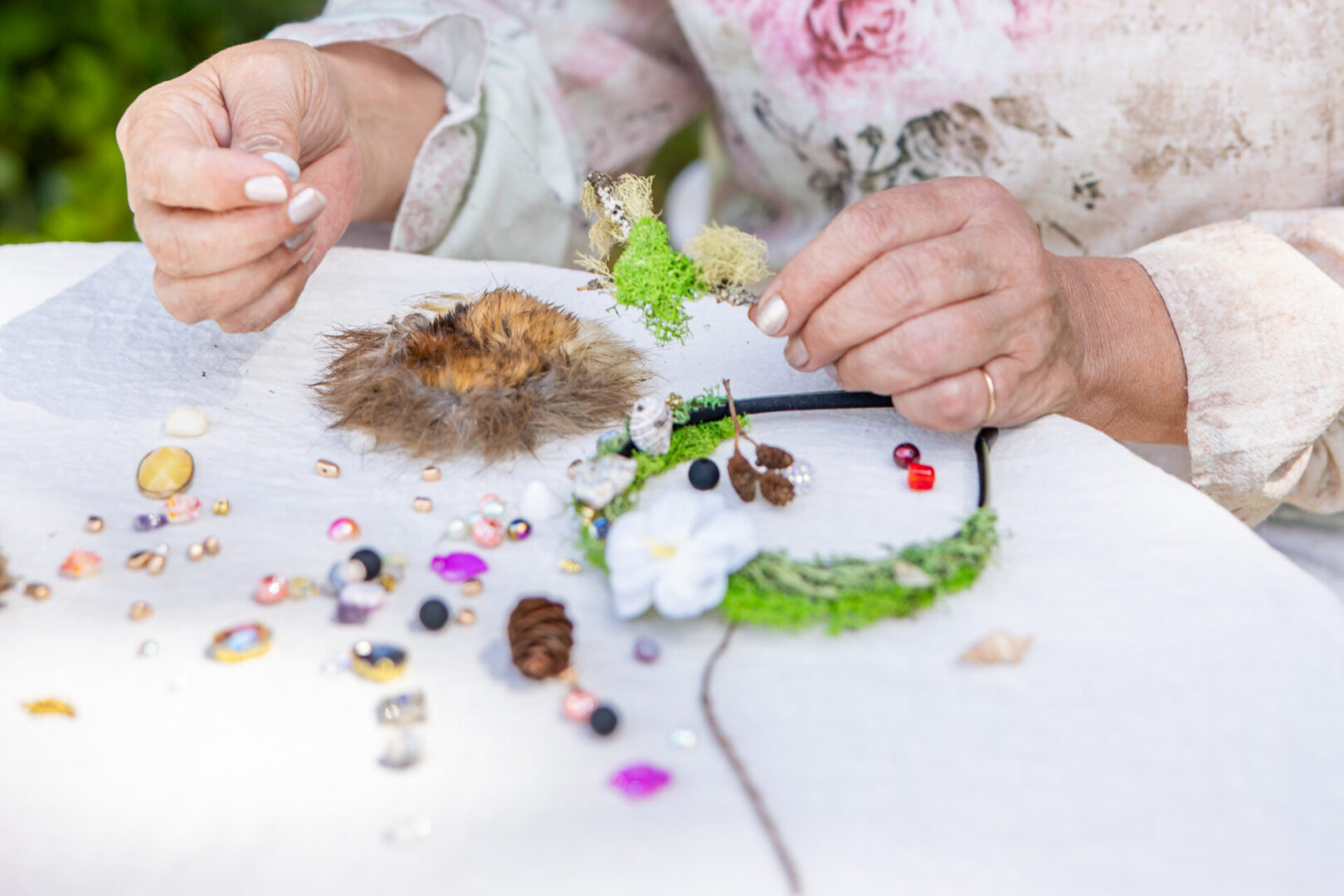 Hands crafting moss, beads, feathers on table